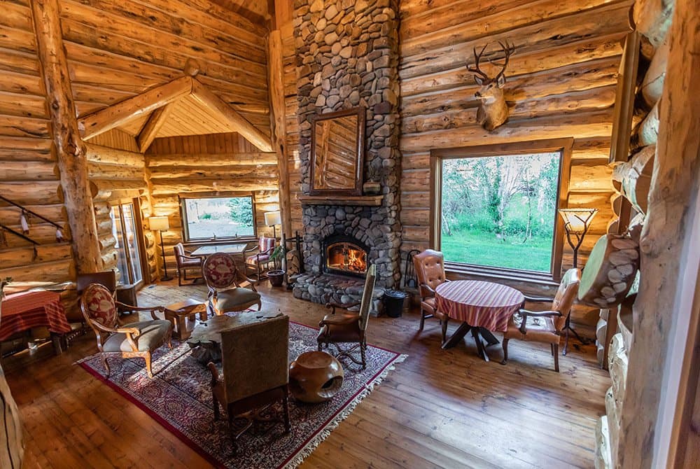 The great room at Bentwood Inn — three-story river-rock fireplace, hand-hewn log walls, Teton view through the picture window